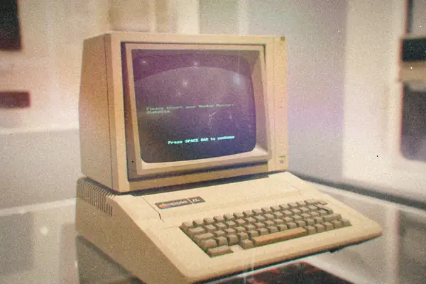 A vintage Apple II computer with green text glowing on its monitor.