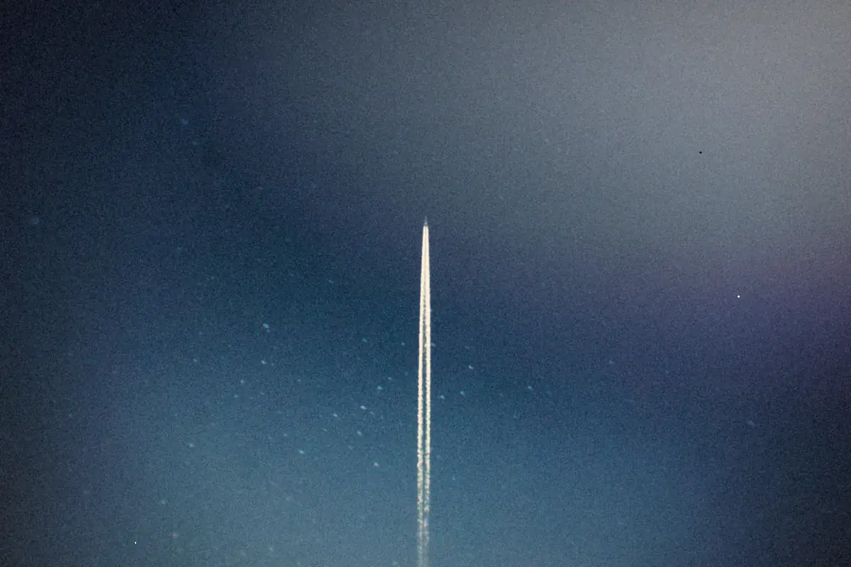 A rocket's trail streaking straight up through a starry night sky.