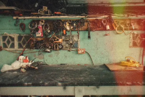 A cluttered old workshop wall with tools and parts hanging above a long workbench.