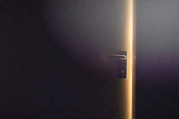 A dark room with a door slightly open and light glowing through.