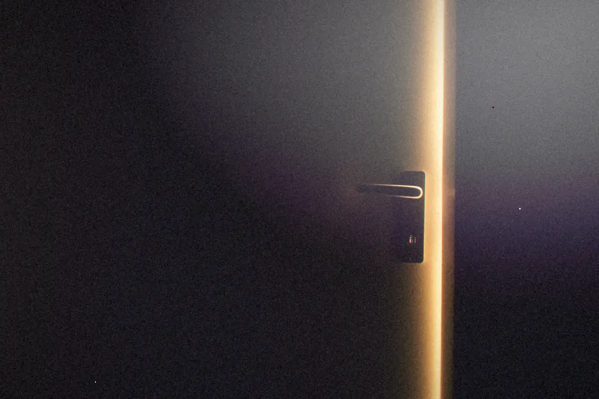 A dark room with a door slightly open and light glowing through.