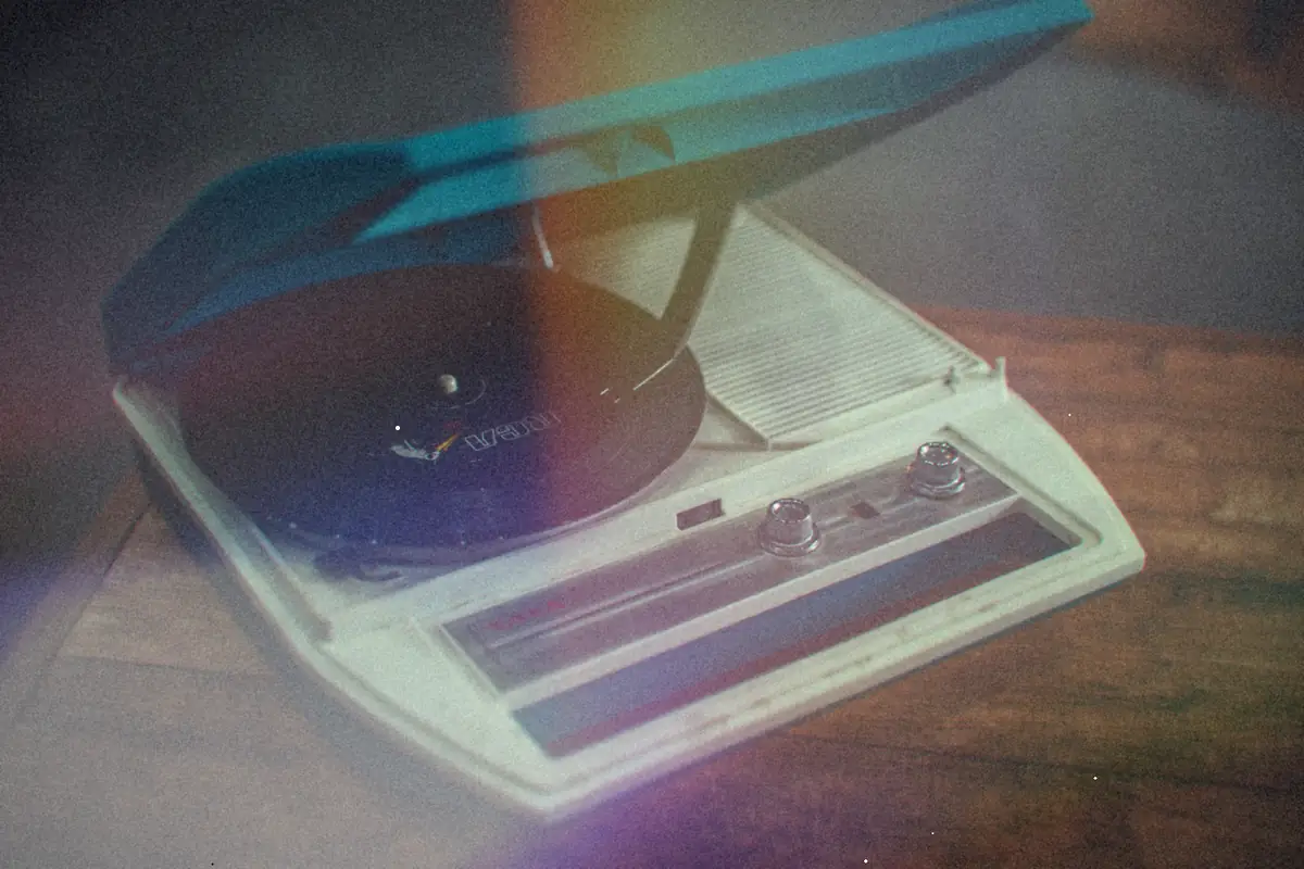 A teal portable record player with a record on it sitting on a wooden table.