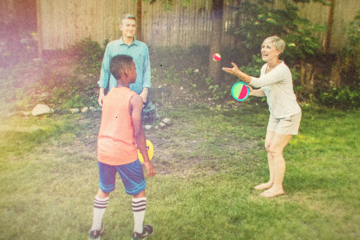 A family tossing a ball around in a grassy backyard on a summer day.