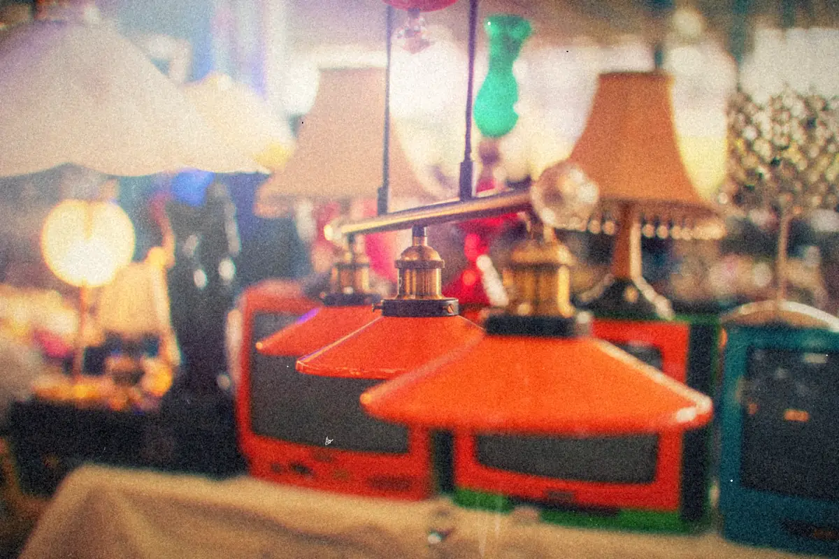 Old lamps and retro television sets piled up at a busy secondhand market stall.
