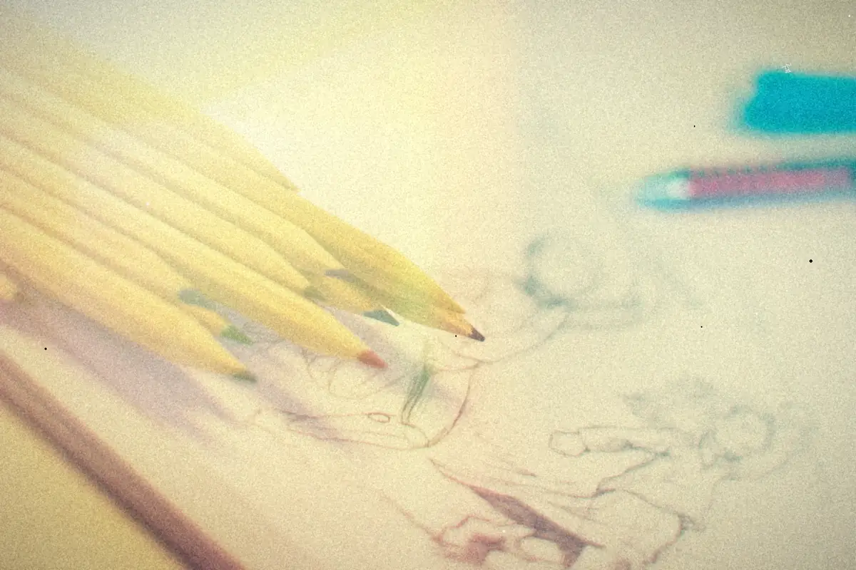 A handful of colored pencils lying on a sketchbook page full of pencil drawings.