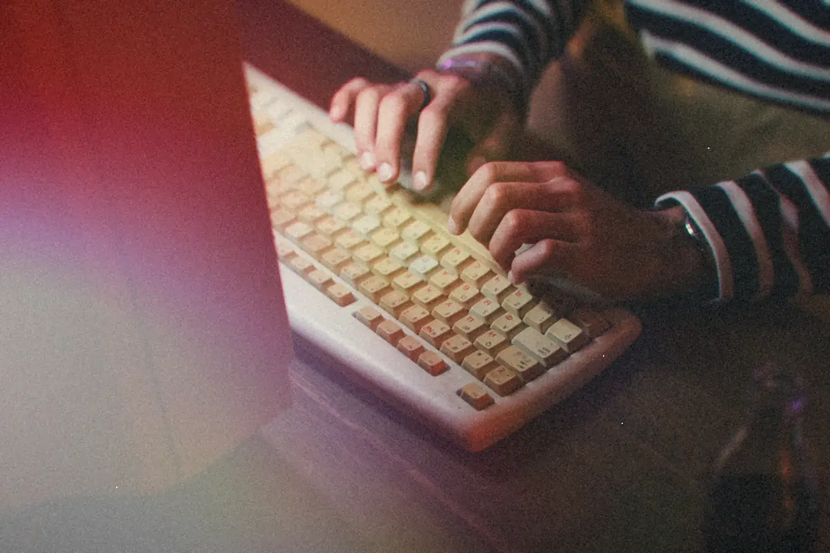 Hands typing on an old beige computer keyboard next to the edge of the monitor.