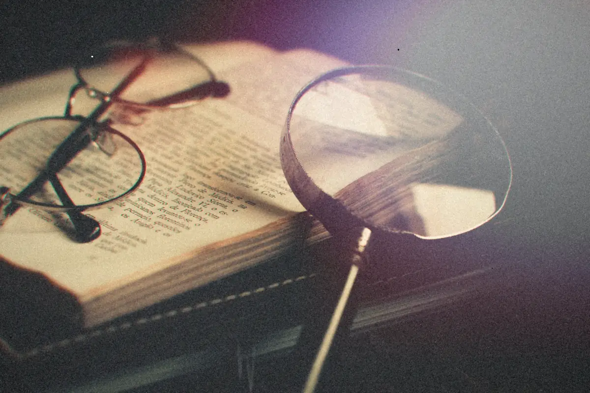 A magnifying glass and reading glasses resting on an open book.