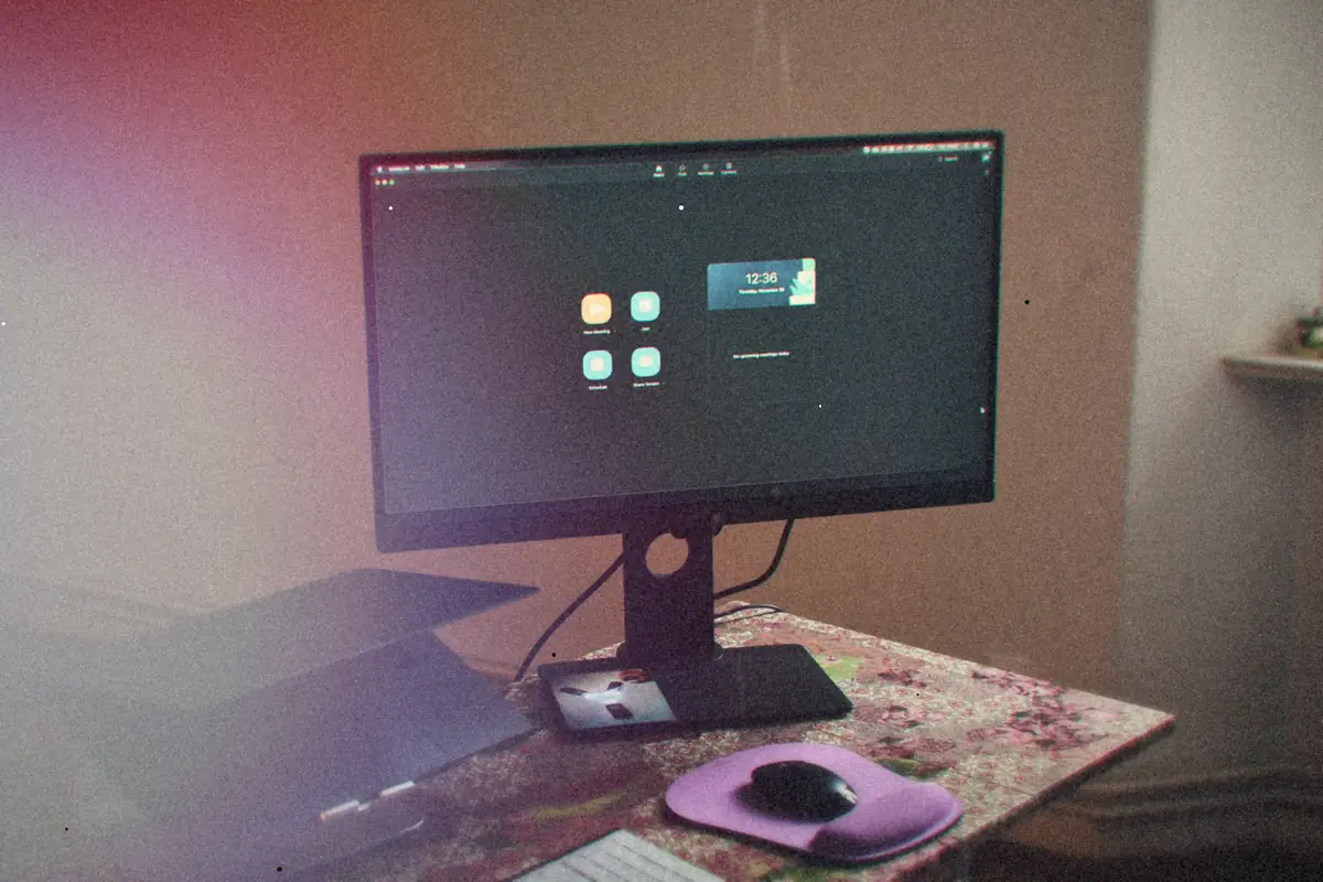 A monitor showing a simple dark desktop, on a small desk with a laptop stand and a purple mouse pad.