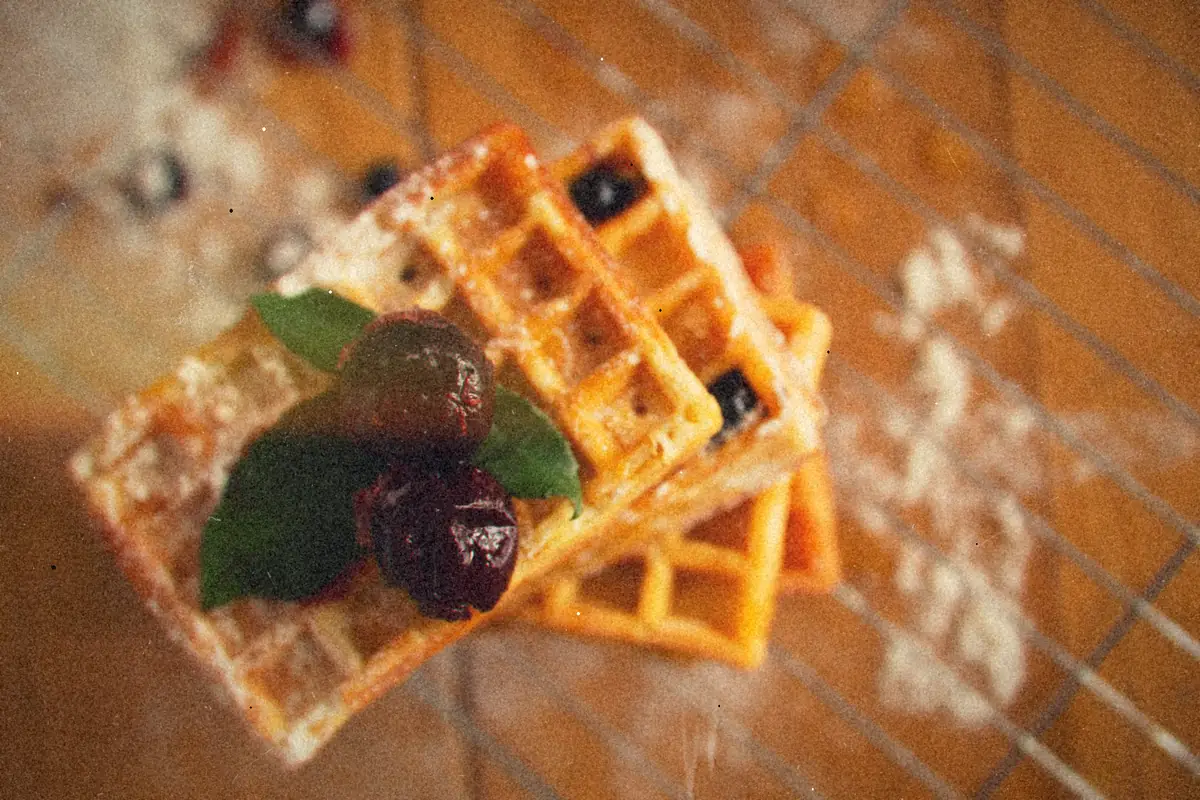 Golden waffles dusted with powdered sugar and topped with cherries and mint on a wire rack.