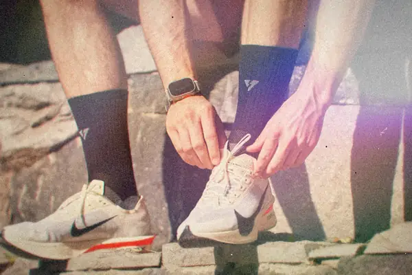 Hands lacing up a pair of running shoes on stone steps in the sun.