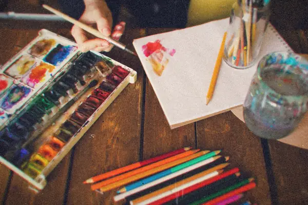 An artist's desk with watercolors, pencils and an open sketchbook.