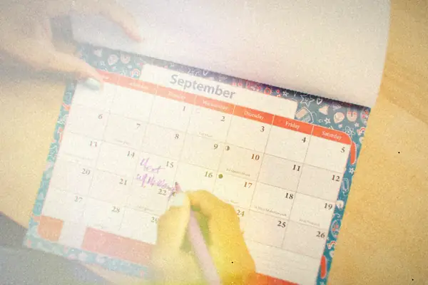 A hand writing a note on a September wall calendar with a purple pen.