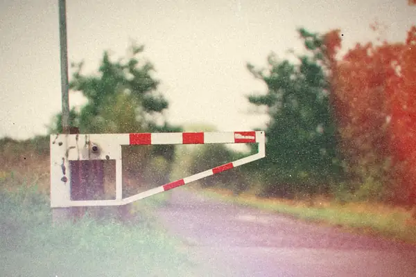 A red and white barrier gate across a quiet country lane lined with trees.