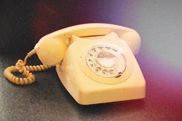 A cream-colored rotary telephone with its coiled cord on a dark surface.