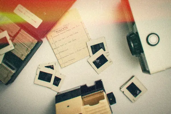 A vintage slide projector with scattered film slides and a handwritten slide list.