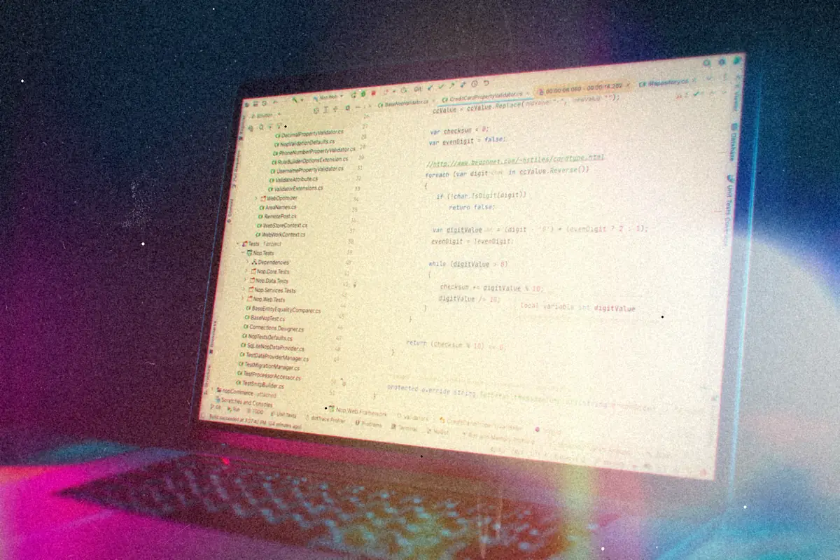 A laptop screen full of code in a light editor theme, lit blue and pink from the side.