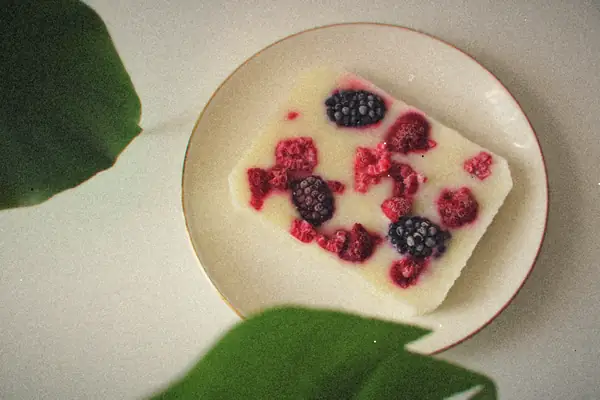 A slab of frozen yogurt bark set with raspberries and blackberries on a white plate.