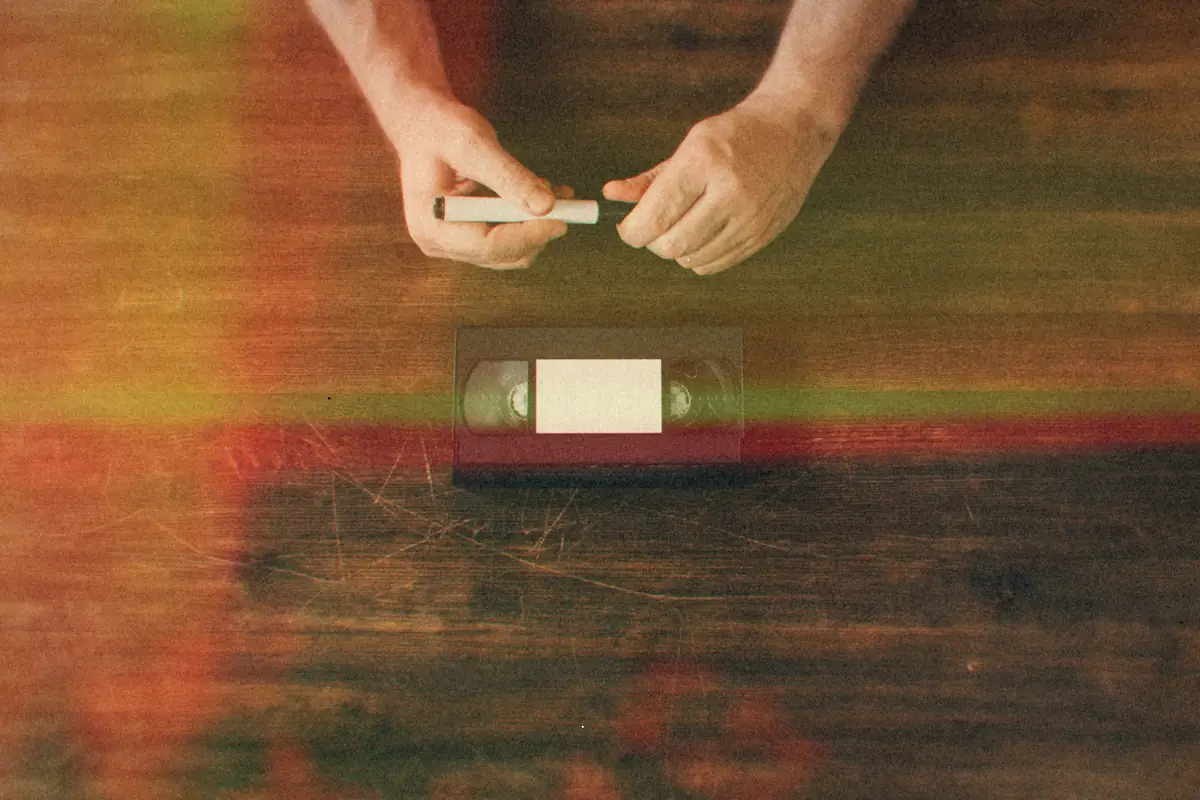 Hands labeling a VHS tape with a marker on a wooden table.