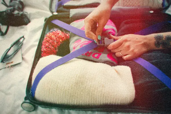 Hands tighten a strap over clothes packed into an open suitcase.